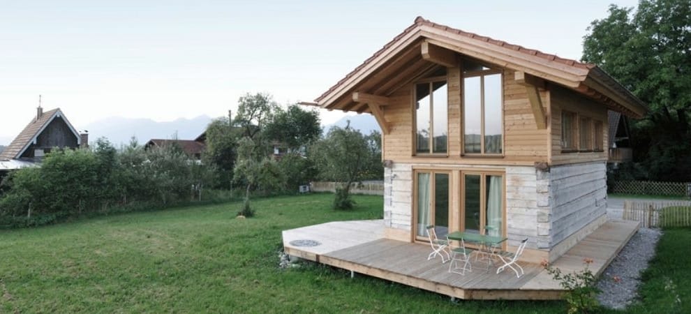 Blockhaus Typ "Grafenaschau" von Artifex mit Terrasse auf einer grünen Wiese vor Berglandschaft