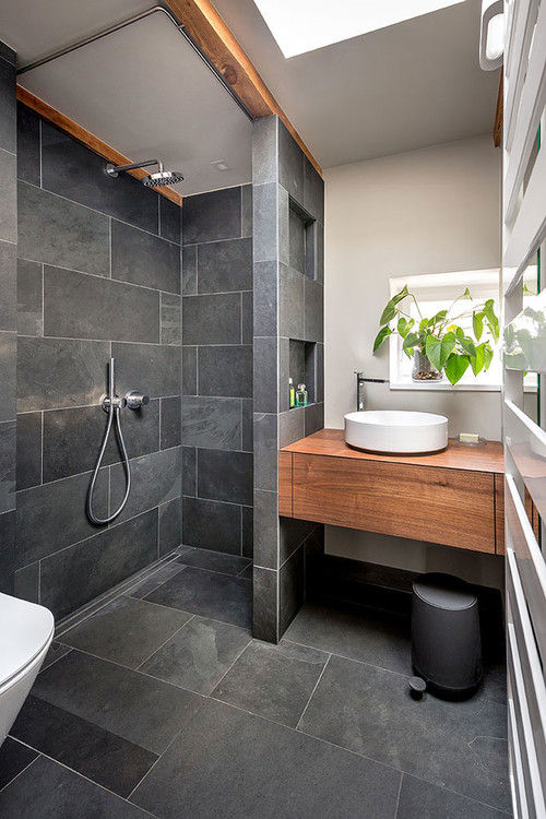Modernes Badezimmer mit einer dunklen Duschkabine, hellem Waschbecken und Holzunterschrank