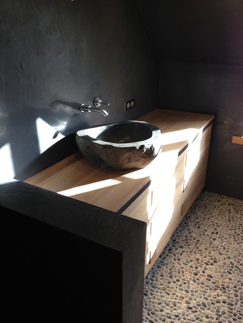 Badezimmer mit Kieselsteinboden, Holzelementen, schwarzer Steinwand und dunklem Waschbecken