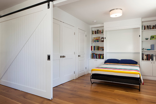 Weiße Schiebetür im Scheunenstil, die ein modernes Regal mit Klappbett verdeckt