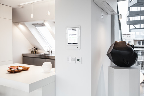 Tablet-Steuereinheit für Smart Home an weisser Wand neben einer Küche mit Dachfenster und schwarzer Skulptur
