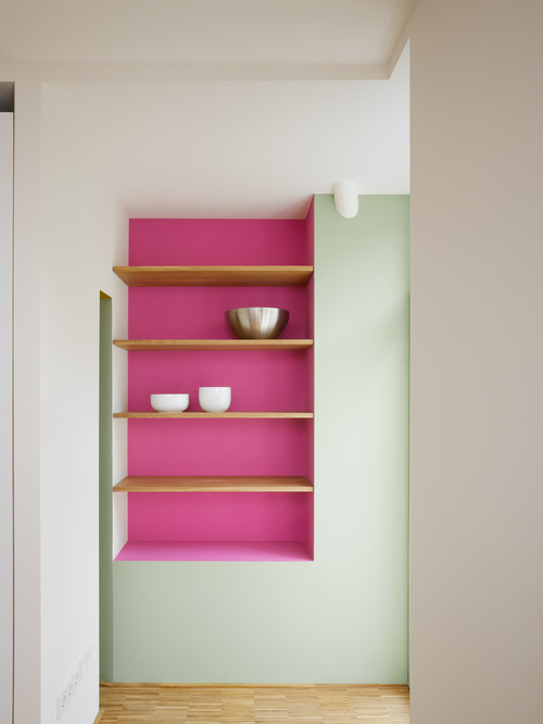 Eine Nische in der Wand mit pinkfarbener Rückseite und hellen Holzregalen, darauf Schalen