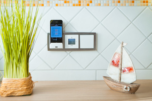 Smartphone in Ladestation, daneben Smart-Home-Steuerung und dekoratives Segelboot auf Holzoberfläche