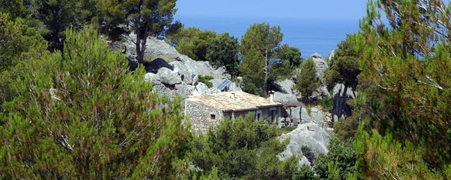 Casita Muleta zwischen Deia und Sóller, umgeben von Felsen und Bäumen, mit Meer im Hintergrund