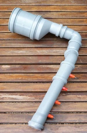 Grauer Hühner-Tränkeautomat aus PVC-Rohren mit Nippeltränken auf einem Holzuntergrund