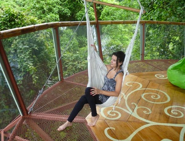 Eine Frau sitzt in einer Hängematte auf der Terrasse des Dschungel-Baumhauses mit Blick in den Urwald