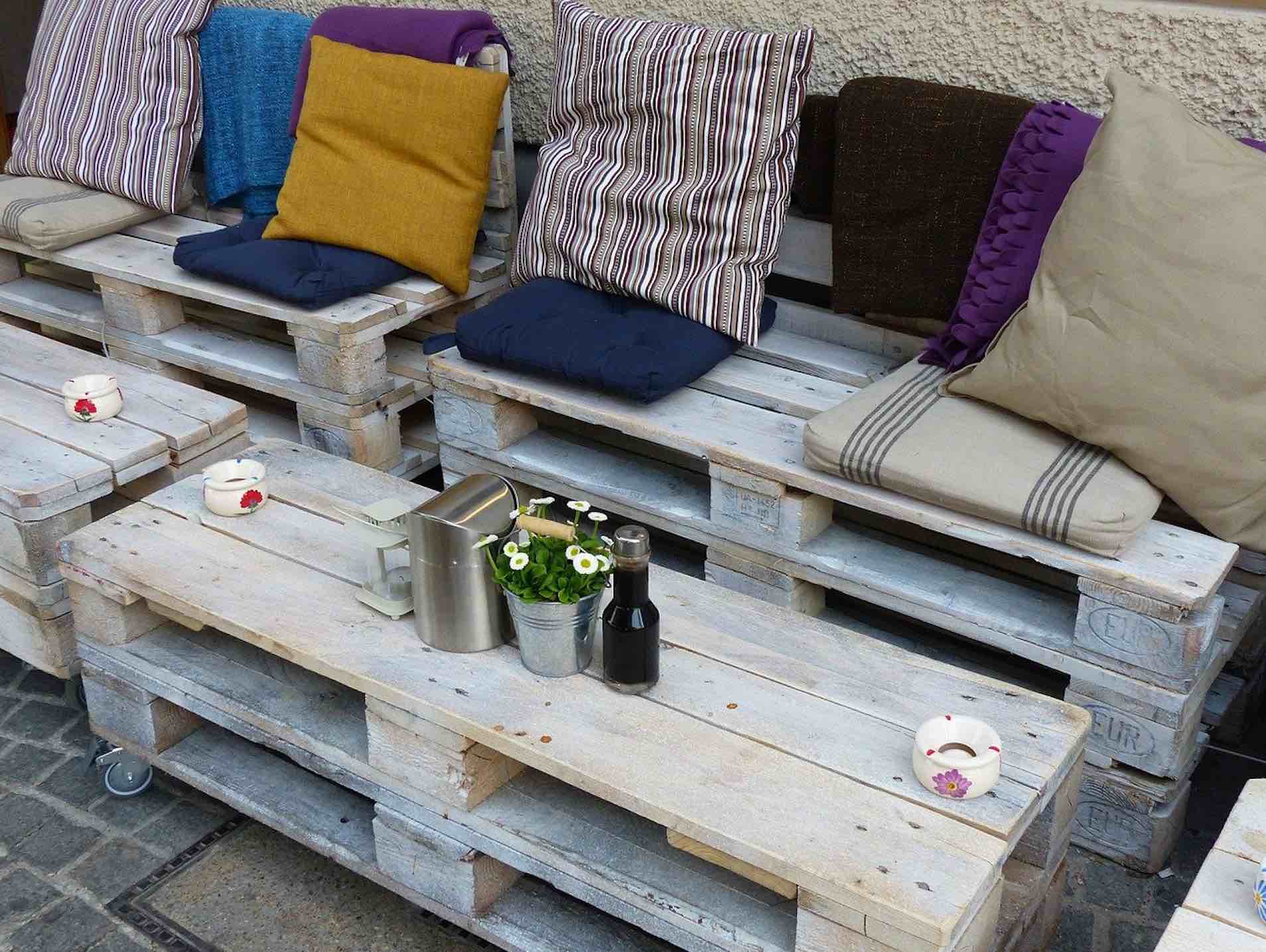 Upcycling-Sitzbank aus Europaletten mit bunter Kissen-Deko und Beistelltisch mit Blumen, Kanne und Flasche