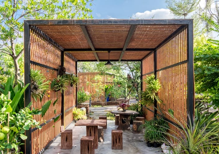 Pergola aus dunklem Holz und einem Dach aus hellem Bambusgeflecht mit Gartenmöbeln und Hängepflanzen