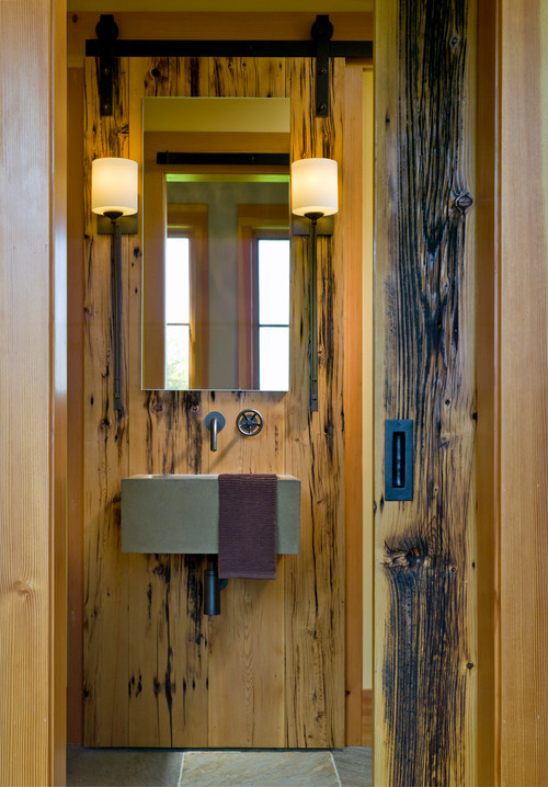 Rustikales Badezimmer mit Holzwänden und Schiebetür, ovalem Becken, Spiegel und zwei Wandlampen