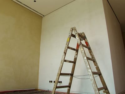 Eine Leiter steht im Raum vor einer teilverputzten Wand, Deckenleisten sind sichtbar