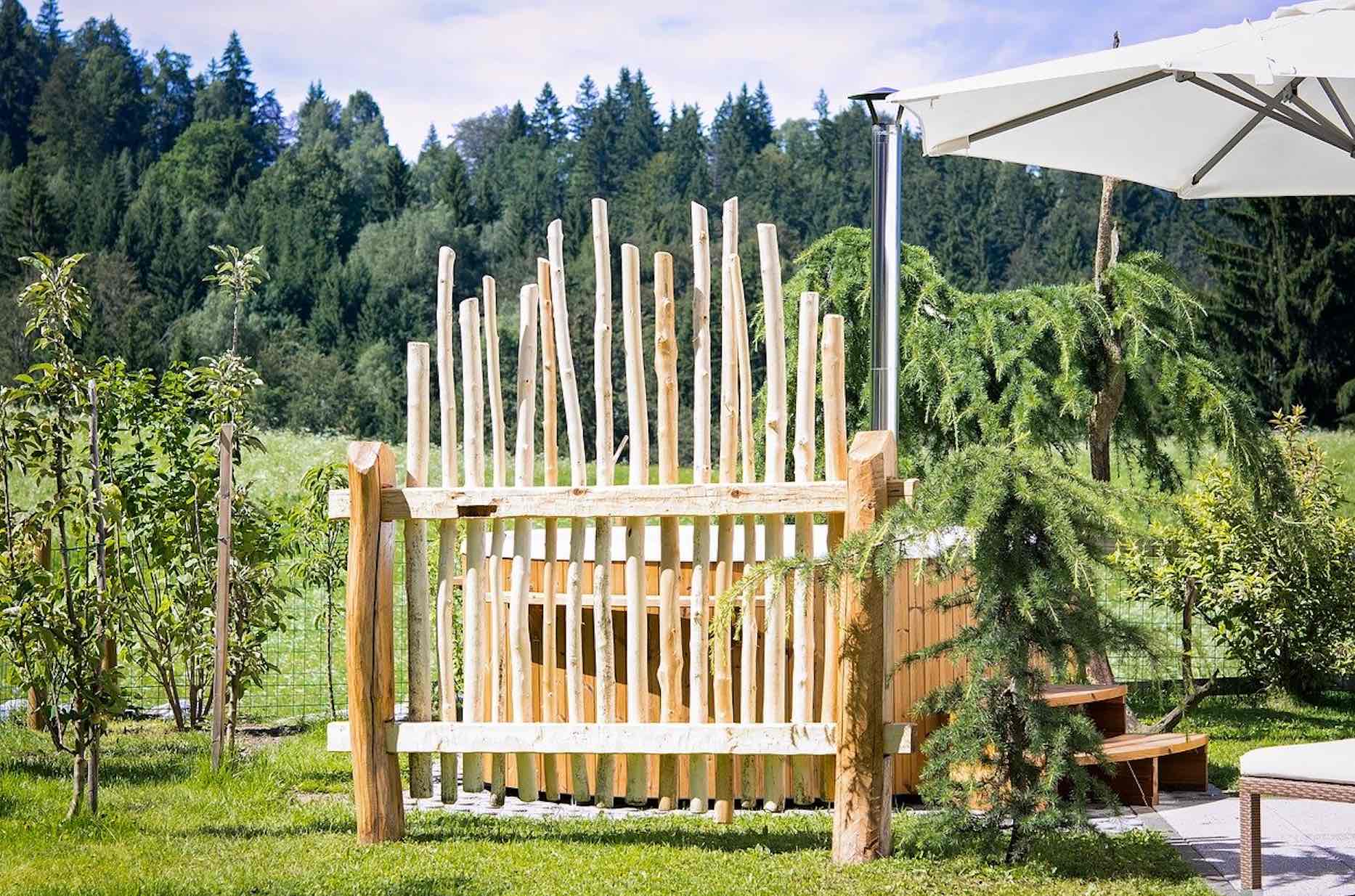 Rustikaler Holzzaun als Sichtschutz für ein Grundstück mit Wald im Hintergrund und modernem Sonnenschirm