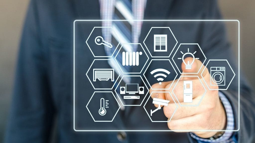 Nahaufnahme einer Hand in Anzug, die auf ein virtuelles Display mit Smart-Home-Icons wie IoT-Symbolen tippt