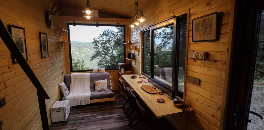 Innenansicht vom Tiny House NimmE „Tiny Fritz“ mit Blick durch die Fenster auf eine bewaldete Berglandschaft
