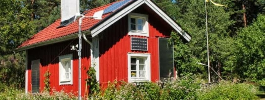 Rot gestrichenes Haus in Schweden mit Solarmodulen, Warmluft-Kollektor und Windrad zur Beheizung