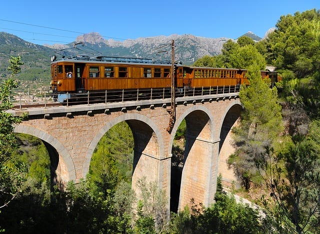 Holzverkleideter Tren de Sóller auf dem Viadukt Pont d'es Tren über das Tal, Bergzüge im Hintergrund