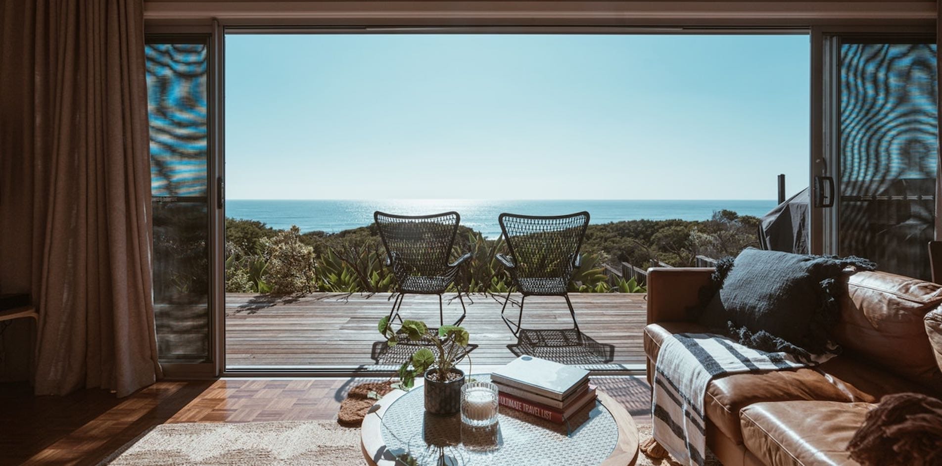 Wohnzimmer mit Meerblick und Terrasse, auf der zwei leere Korbstühle stehen