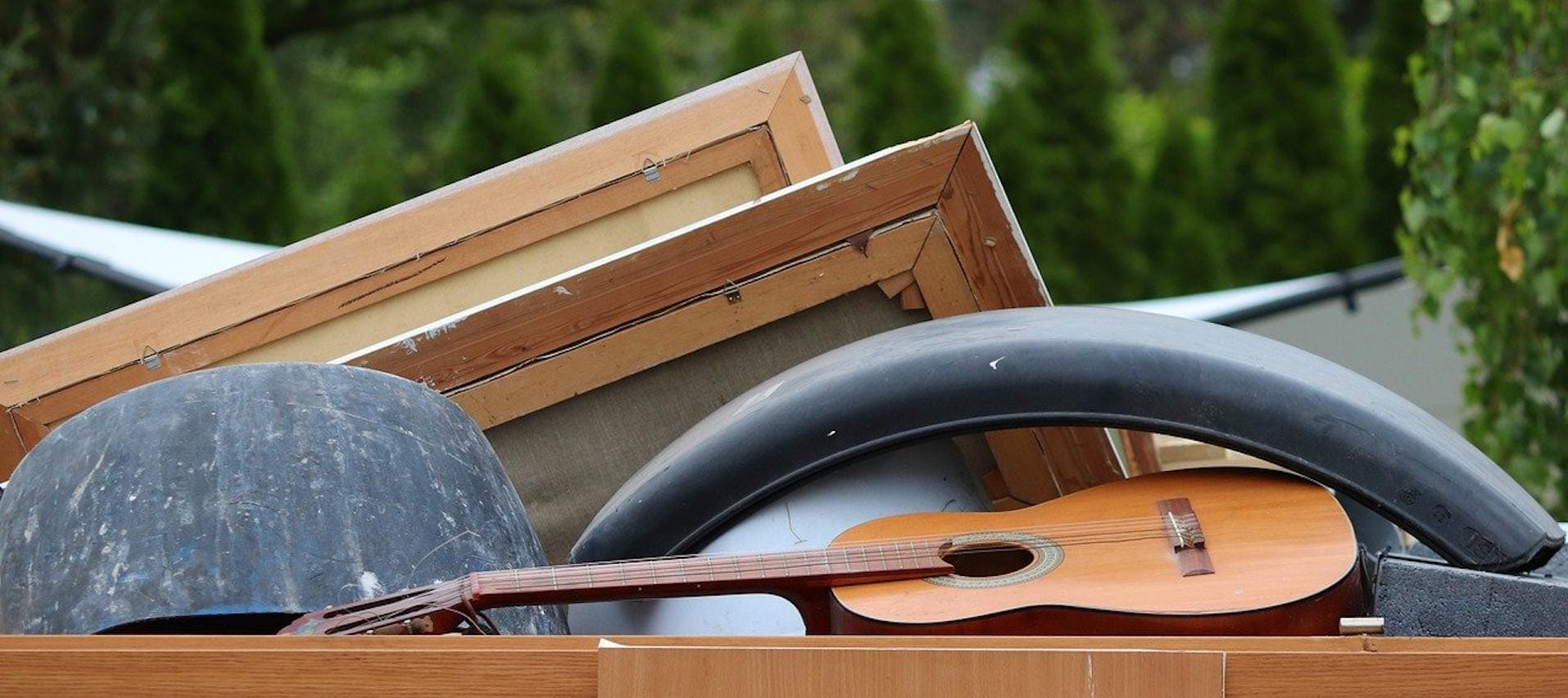 Eine braune Gitarre, eine graue Halbkugel und zwei Bilderrahmen neben einem schwarzen Kotflügel aufeinander gestapelt