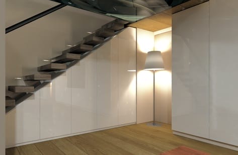 Heller Raum mit Holzfußboden, einer Holztreppe und Einbauschränken. Eine Stehlampe leuchtet eine Nische aus