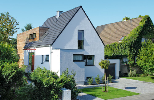 Modernisiertes Siedlungshaus mit weißer Fassade und Holzverkleidung, daneben ein mit Efeu bewachsenes Haus (Foto: Elkin + Bro