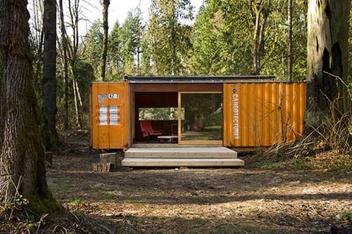 Oranger Seecontainer ausgebaut zum Haus mit Glasfront mitten in einem Waldstück