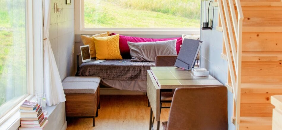 Innenansicht eines Modulhauses als Büro mit Laptop, Büchern, Tisch und zwei Stühlen sowie einem Schlafsofa