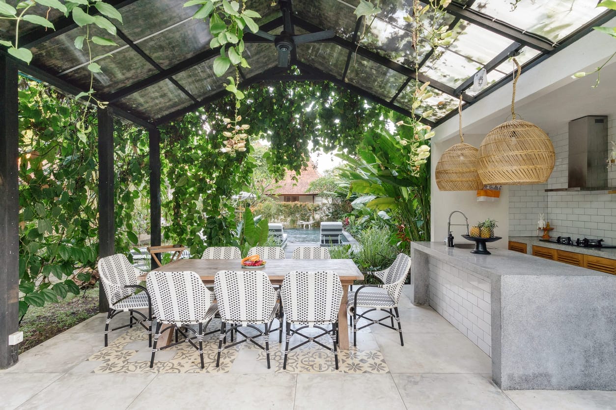 Große, offene überdachte Terrasse mit Esstisch und Stühlen, von Pflanzenranken bewachseneschen, in der Ecke eine gemauerte Au