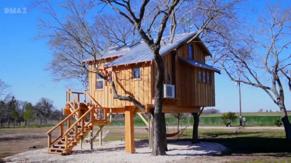 Baumhaus in Oregon. Holzhütte mit Metall-Dach, Fenster, großer Treppe und Balustraden, umringt von Bäumen (DMAX TV)