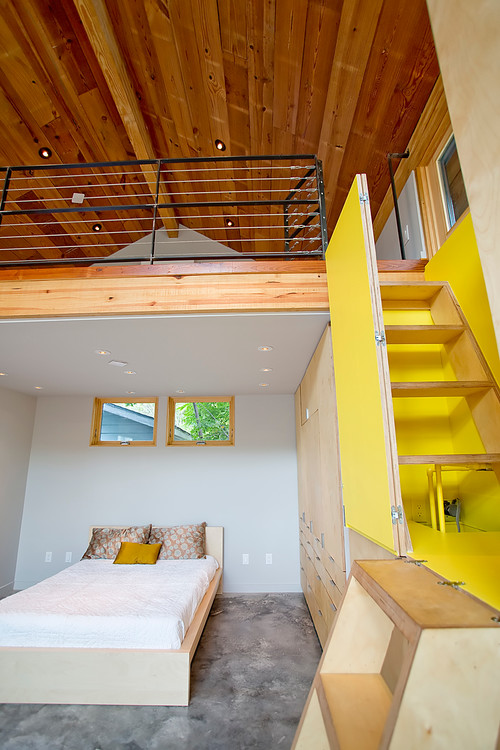 Schlafzimmer mit poliertem Betonboden, Holzbett, gelber Treppe und Galerie