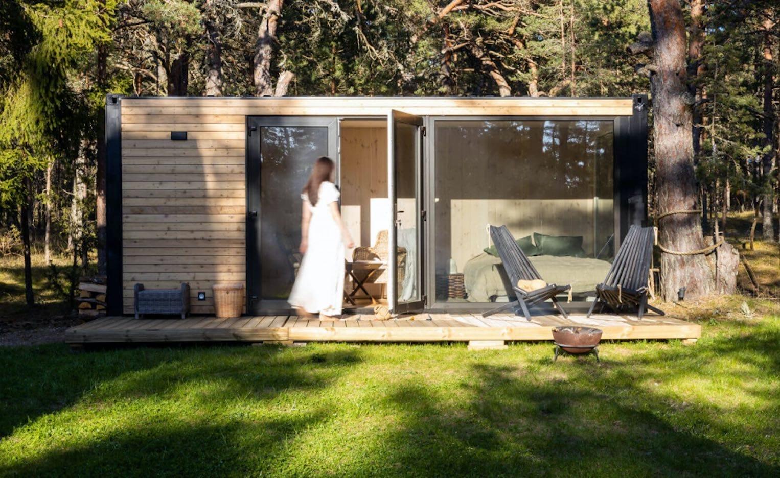 PopUpHuts Containerhaus aus Holz mit Panoramafenstern und Terrasse. Eine Person betritt das Haus