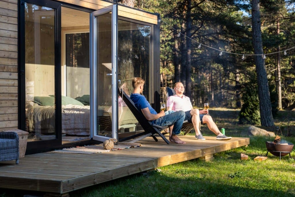 Zwei Männer sitzen auf einer Holzterrasse vor einem PopUpHut und trinken Wein