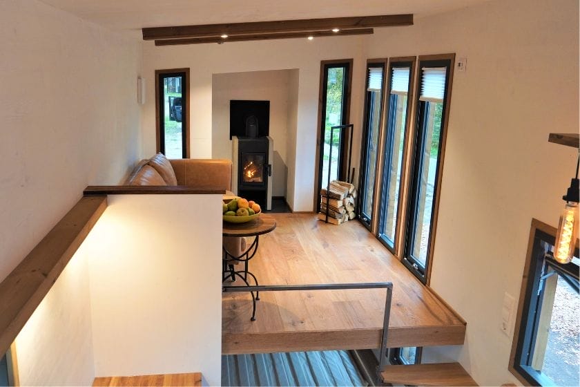 Blick von einer Empore in den Wohnbereich eines modernen Tiny Houses mit Kamin und bodentiefen Fenstern