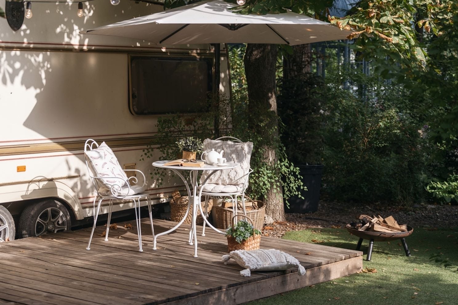 Kleine Holzterrasse am Tiny House, gedeckter Tisch mit Stühlen unter einem Sonnenschirm in Gartenszenerie