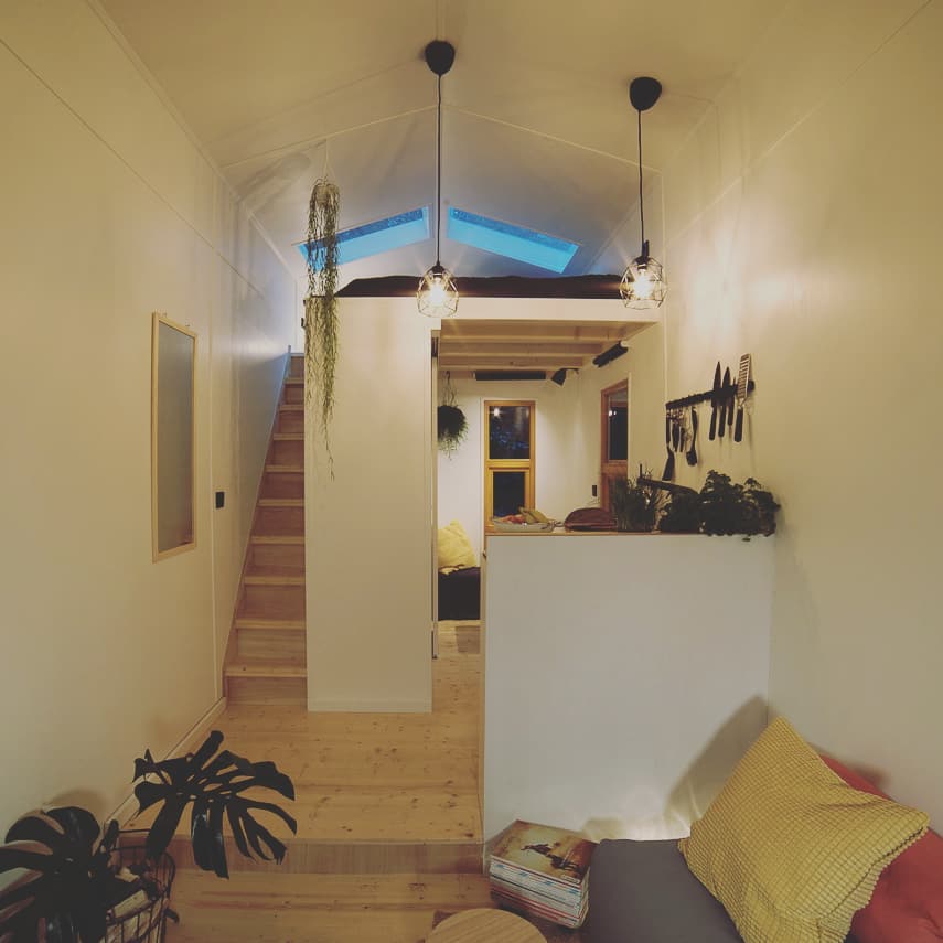 Innenansicht vom Tiny Guesthouse mit einer Kücheninsel, einer Sitzecke und einer Holztreppe, die zu einem Dachfenster führt