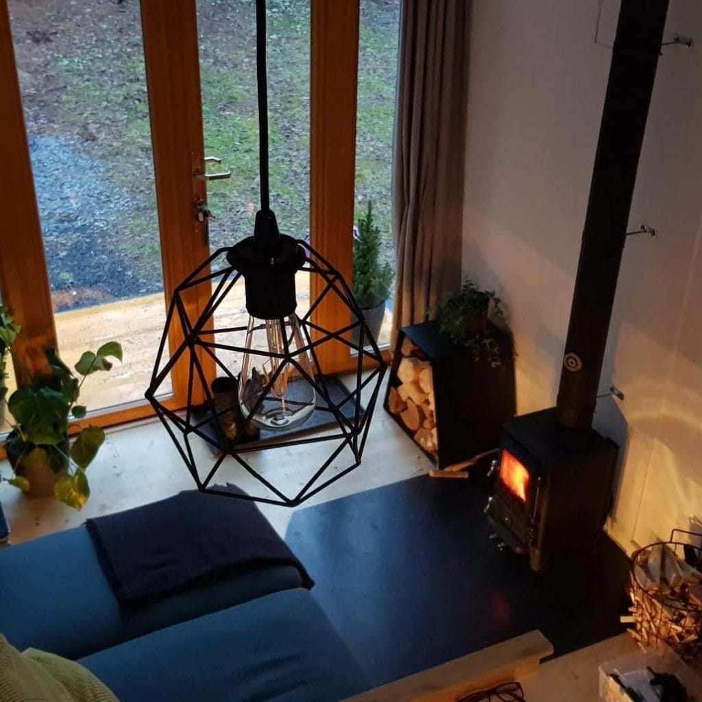 Ein Tiny Escape Wohnzimmer mit Hobbit-Holzofen, Holzscheiten und großer Fensterfront