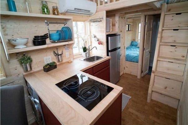 Miniküche in Holzoptik mit moderner Kochplatte und Spüle, kleiner Kühlschrank und angrenzendem Schlafbereich