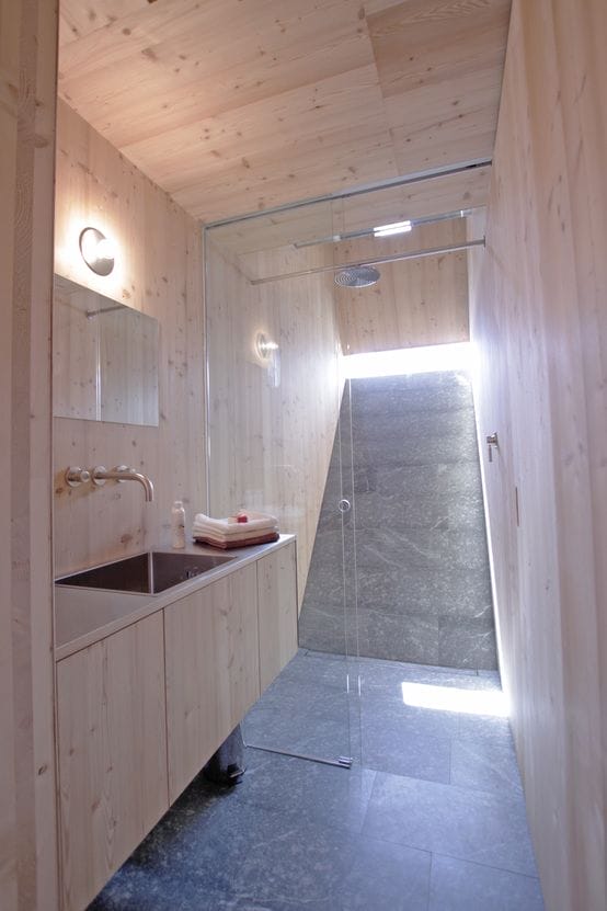 Badezimmer im „Ufogel“: Helles Holz an Wänden und Decke, dunkle Fliesen, Regendusche und Waschbecken mit Spiegel