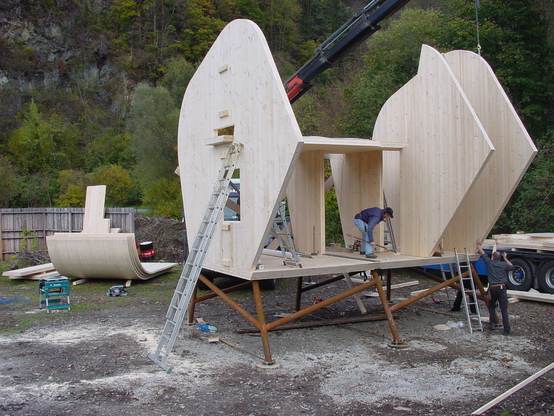 Bau des Ufogels aus Brettsperrholz und Leimholz, mit einem Kran, der Elemente platziert, und Bauarbeitern am Werk