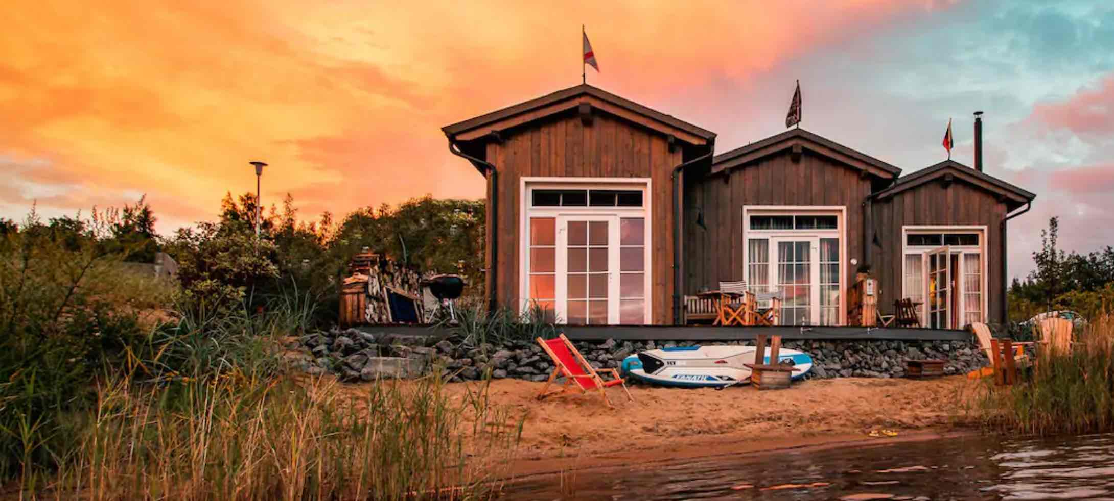 Holz-Tiny Houses am Sandstrand mit Blick auf ein Gewässer im Sonnenuntergang
