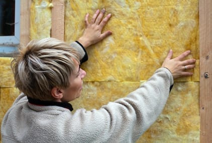 Eine Person bringt gelbe Dämmplatten aus Mineralwolle an einer Holzwand an