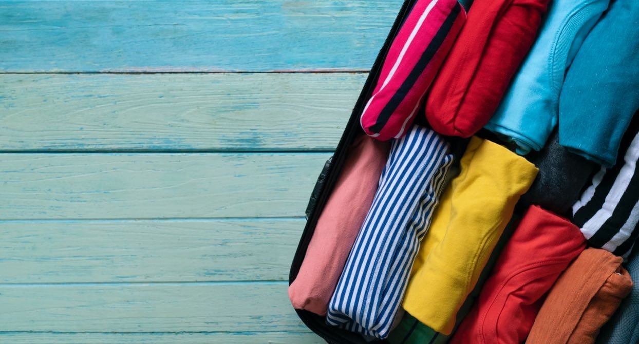 Offener Koffer mit nach der KonMari-Methode gerollter, farbiger Kleidung auf einem Holzboden