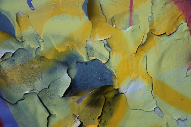Abblätternde gelbe Farbe auf einer blauen Wand mit darunter liegenden Rissen