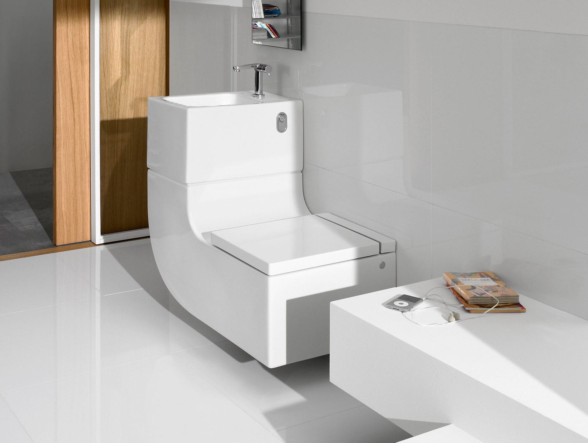 Toilette mit integriertem Waschbecken zur Wassernutzung, dahinter eine Holztür und weiße Fliesen Fliesen