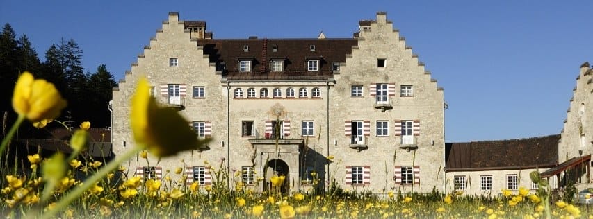 Gesamtansicht des Hotels Kranzbach, ein historisches Schlossgebäude, umgeben von einer gelb blühenden Wiesenlandschaft