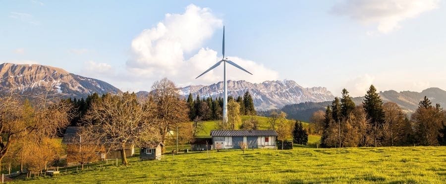 Windkraftanlage auf einer grünen Wiese mit Bergen und Wald im Hintergrund