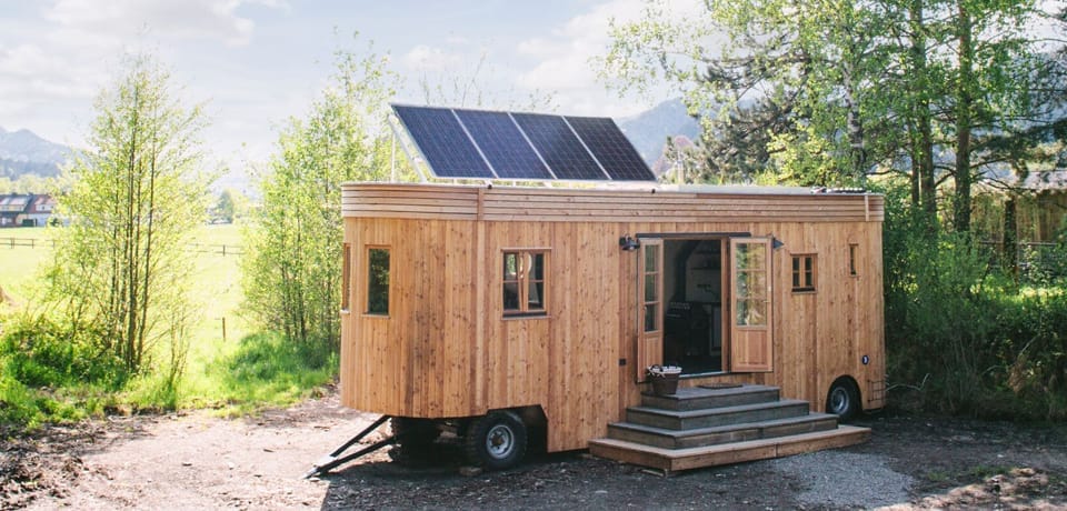 Holz-Tiny-House mit Solarpaneelen auf dem Dach und Treppe am Eingang auf einer Wiese