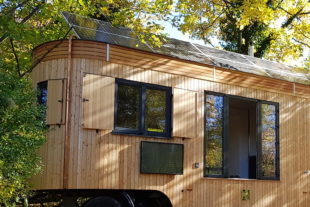 Holzverkleidetes Tiny House mit Solarmodulen auf dem Dach, umgeben von herbstlichen Bäumen