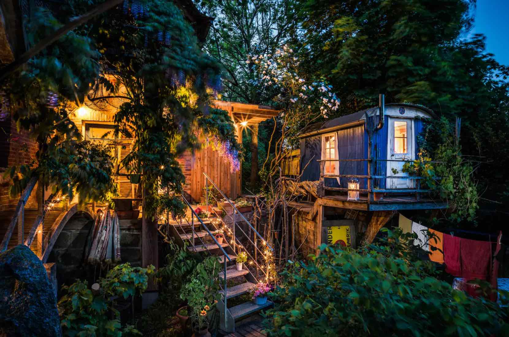 Ein Tiny House aus einem alten Zirkuswagen umgeben von Bäumen und Büschen im Garten