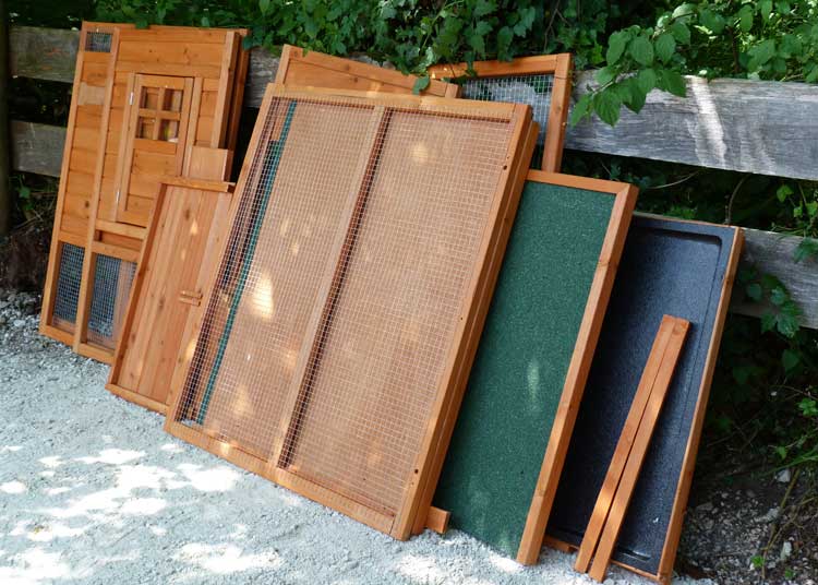 Einzelne Bauteile eines günstigen Hühnerstall-Bausatzes, darunter Holzwände, Drahtgitter und Bodenplatten