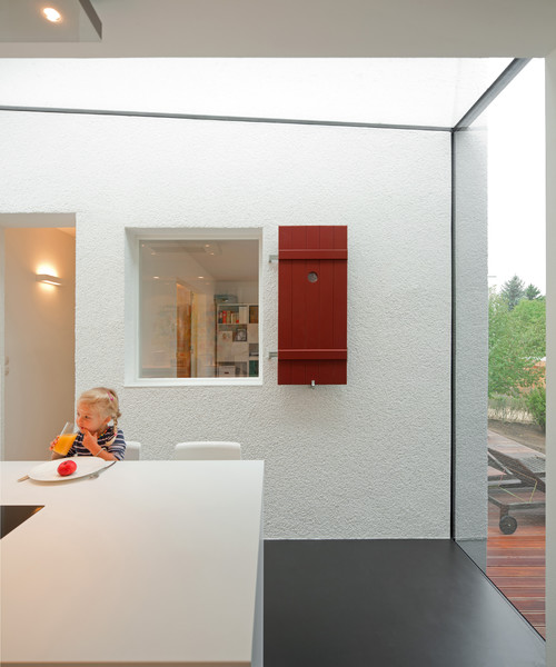 Innenaufnahme eines modernen Anbaus mit großem Fenster, davor ein Kind am Esstisch, draußen eine Holzterrasse