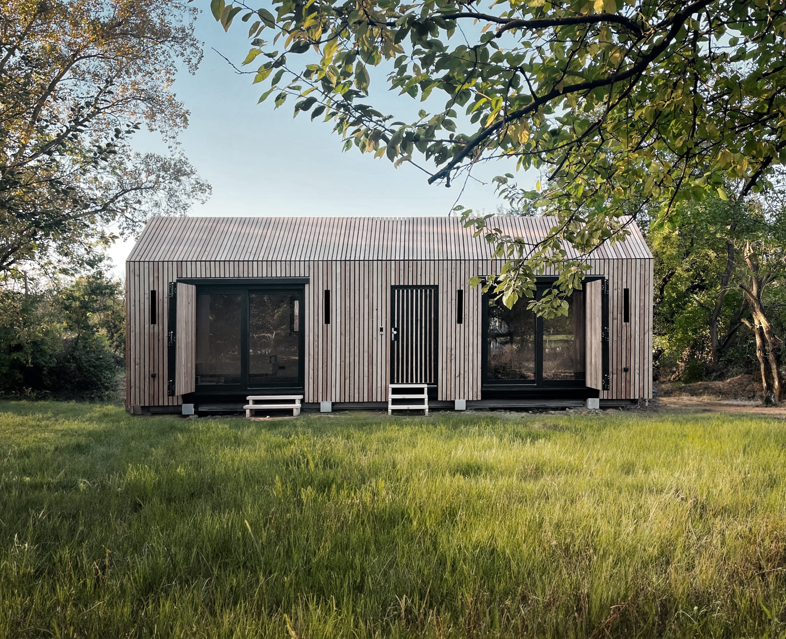 Die Tinca Cabin, ein nachhaltiges Tiny House aus Holz, steht auf einer grünen Wiese unter blauem Himmel